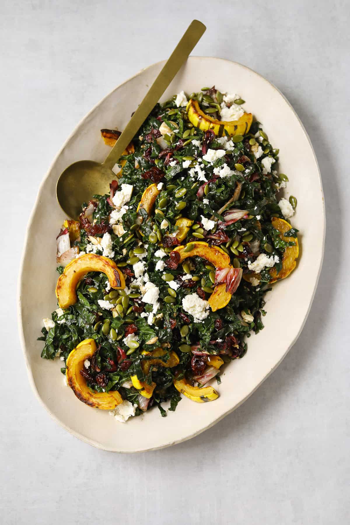 roasted delicata squash salad on a large oval platter with a gold spoon on a light grey background 