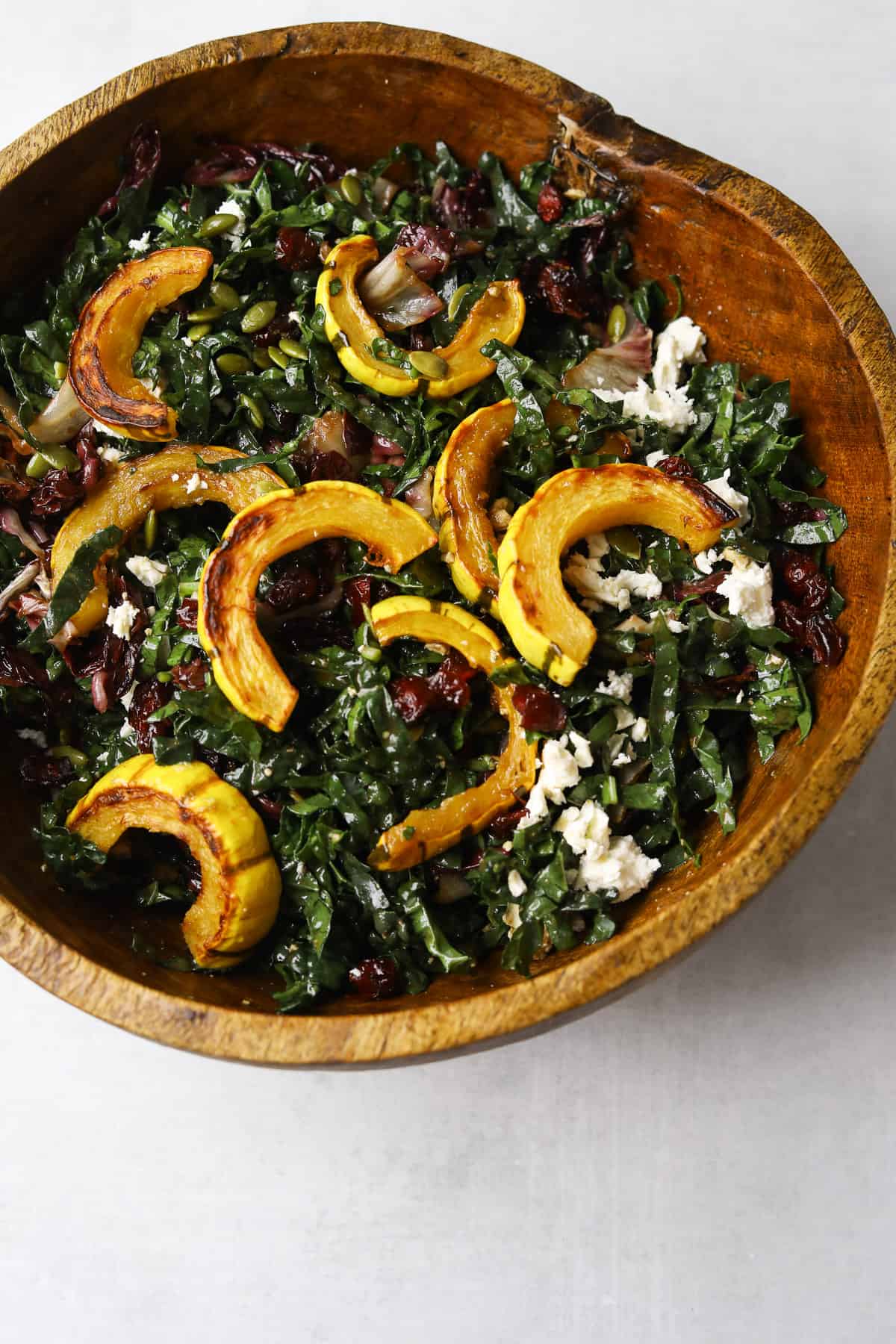 a wooden salad bowl filled with roasted delicata squash salad 