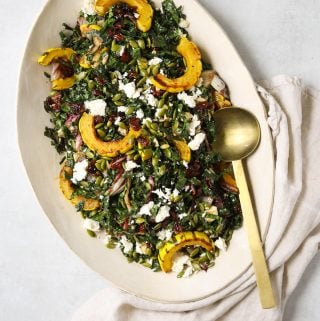 a large oval platter filled with roasted delicata squash salad, a gold spoon and linen napkin