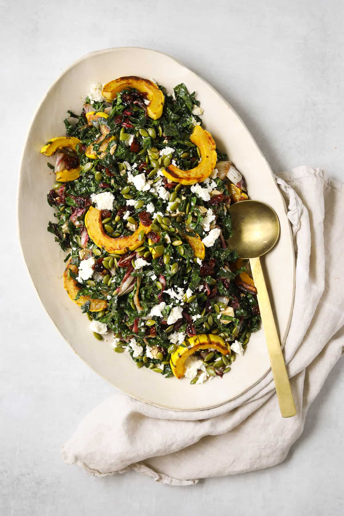 a large oval platter filled with roasted delicata squash salad, a gold spoon and linen napkin