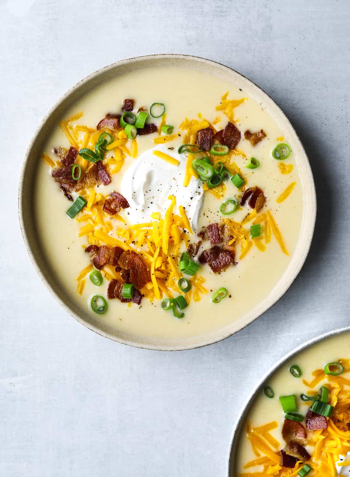 a bowl of potato soup topped with shredded cheddar cheese, bacon, sour cream and sliced green onion.