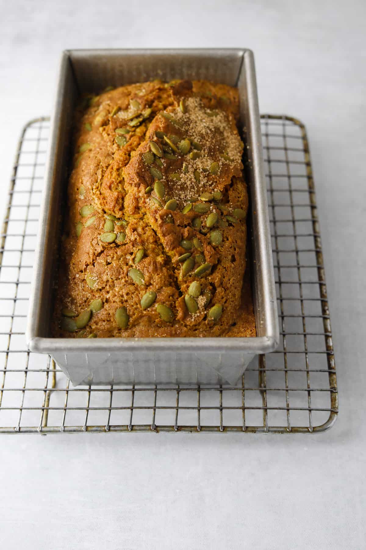 pumpkin bread in a loaf pan on top of a cooling rack on a blue background 