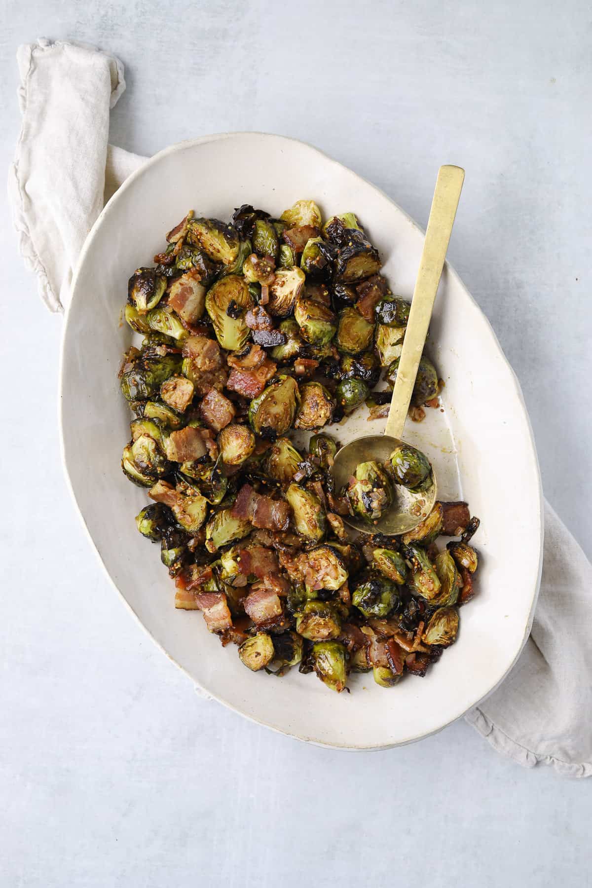 a large white platter filled with roasted Brussel Sprouts with bacon vinaigrette and a gold spoon