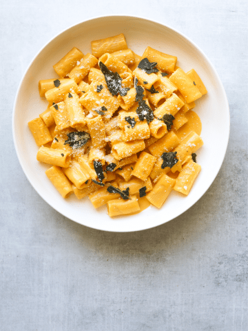 a white bowl filled with creamy pumpkin rigatoni and topped with crispy fried sage