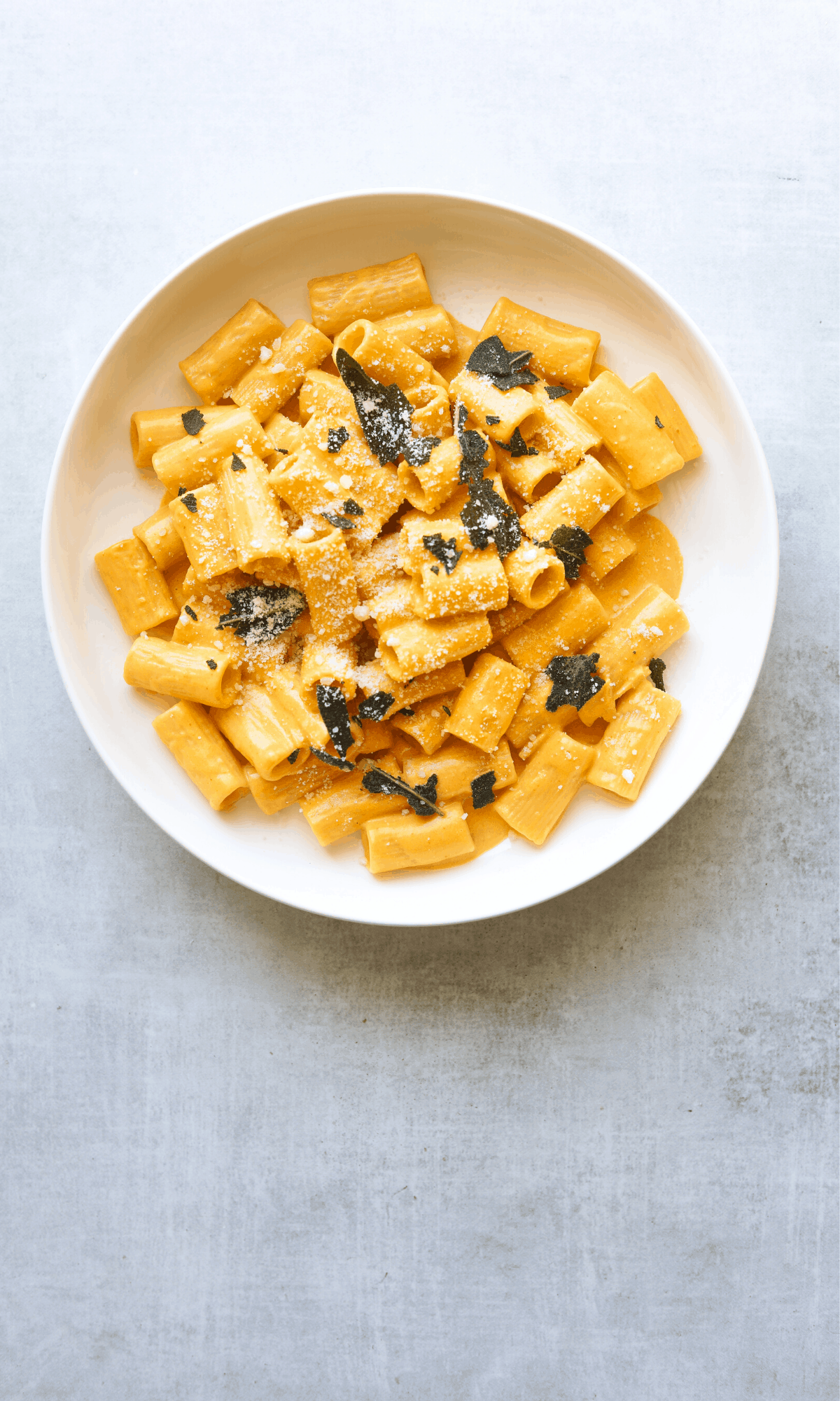 a white bowl filled with creamy pumpkin rigatoni and topped with crispy fried sage