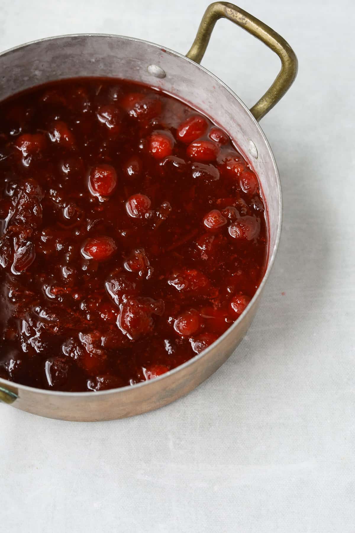 a copper sauce pot filled with cranberry sauce on a blue background 
