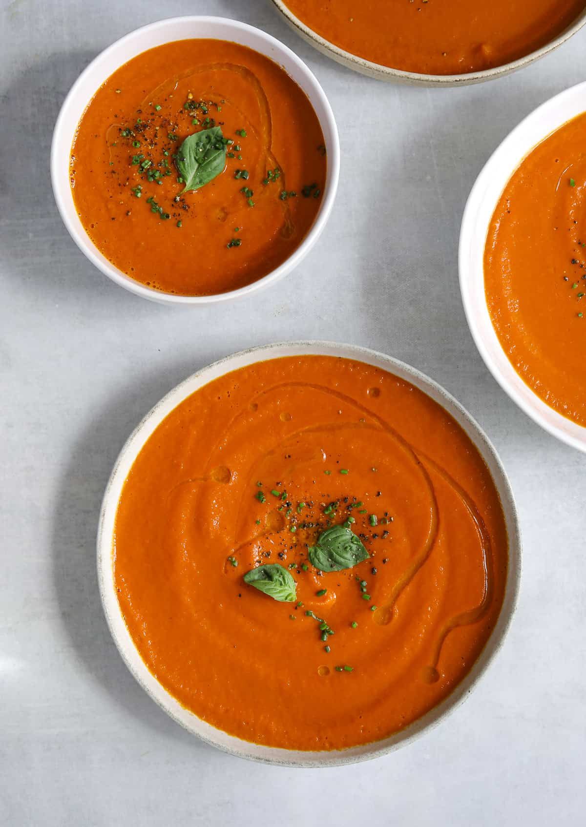 a bowl of creamy vegan tomato soup with a drizzle of olive oil, chives and fresh basil