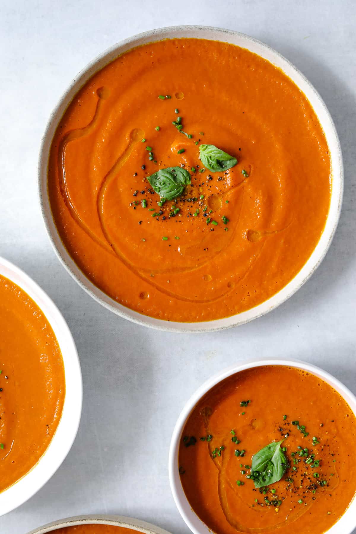 three bowls of creamy vegan tomato soup topped with a drizzle of olive oil, chives, black pepper and basil leaves