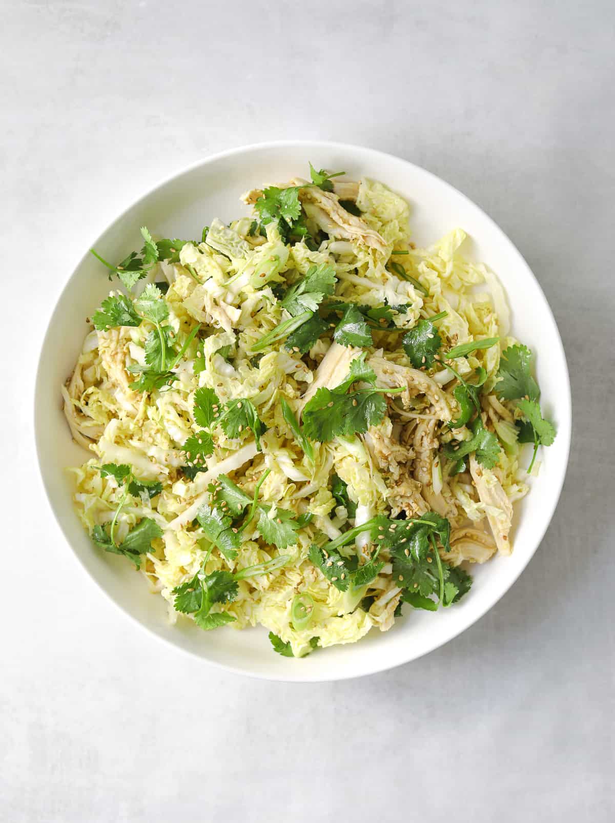 a white bowl filled with a shedded cabbage salad with chicken, sesame seeds and miso ginger dressing