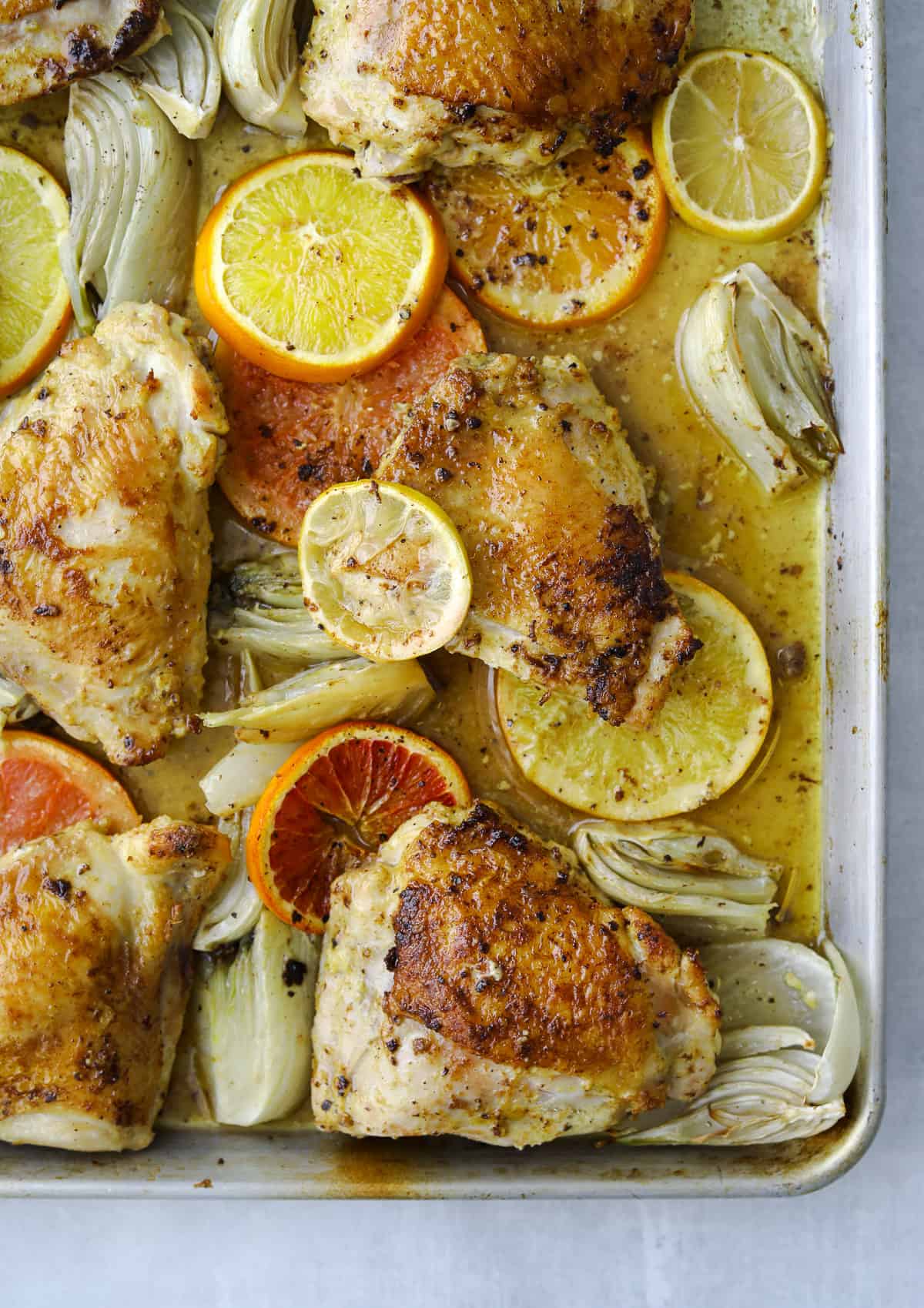 golden brown roasted chicken thighs with citrus, fennel, olive oil on a baking tray