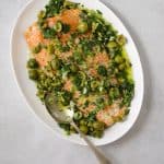 a large white platter of salmon topped with a fresh green sauce of crushed olives, parsley and green onion