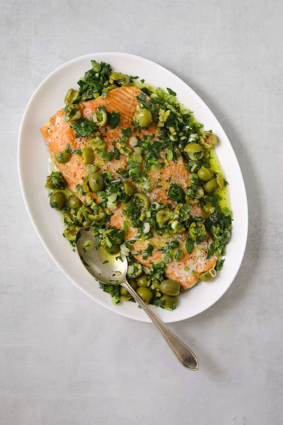 a large white platter of salmon topped with a fresh green sauce of crushed olives, parsley and green onion