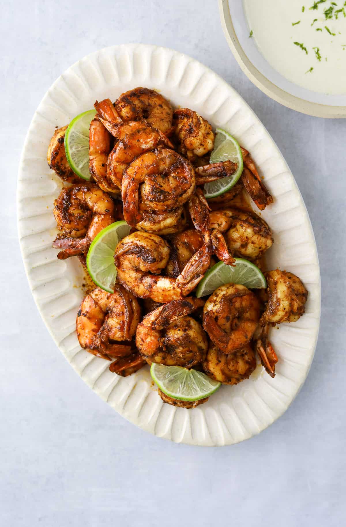 a white oval platter of blackened shrimp with lime slices and a bowl of garlic-lime aioli on the side