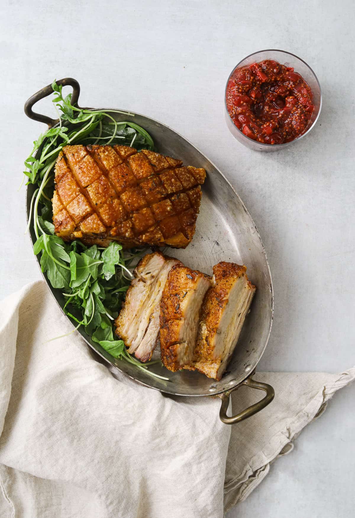 crispy roasted pork belly in an oval copper pan with arugula and a bowl of cranberry mustard 