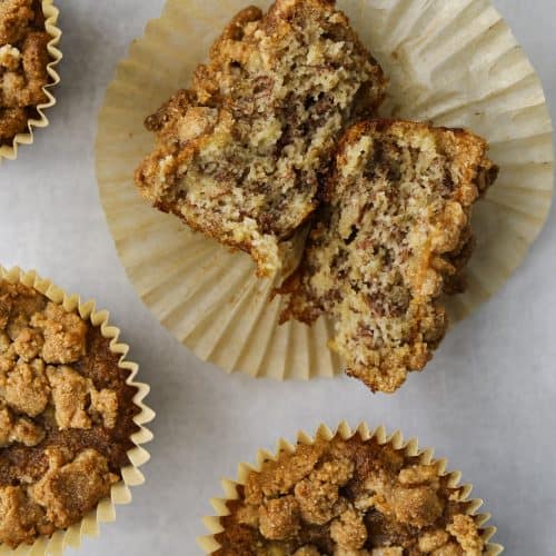 four almond flour banana muffins, one cut in half revealing a moist and fluffy center.