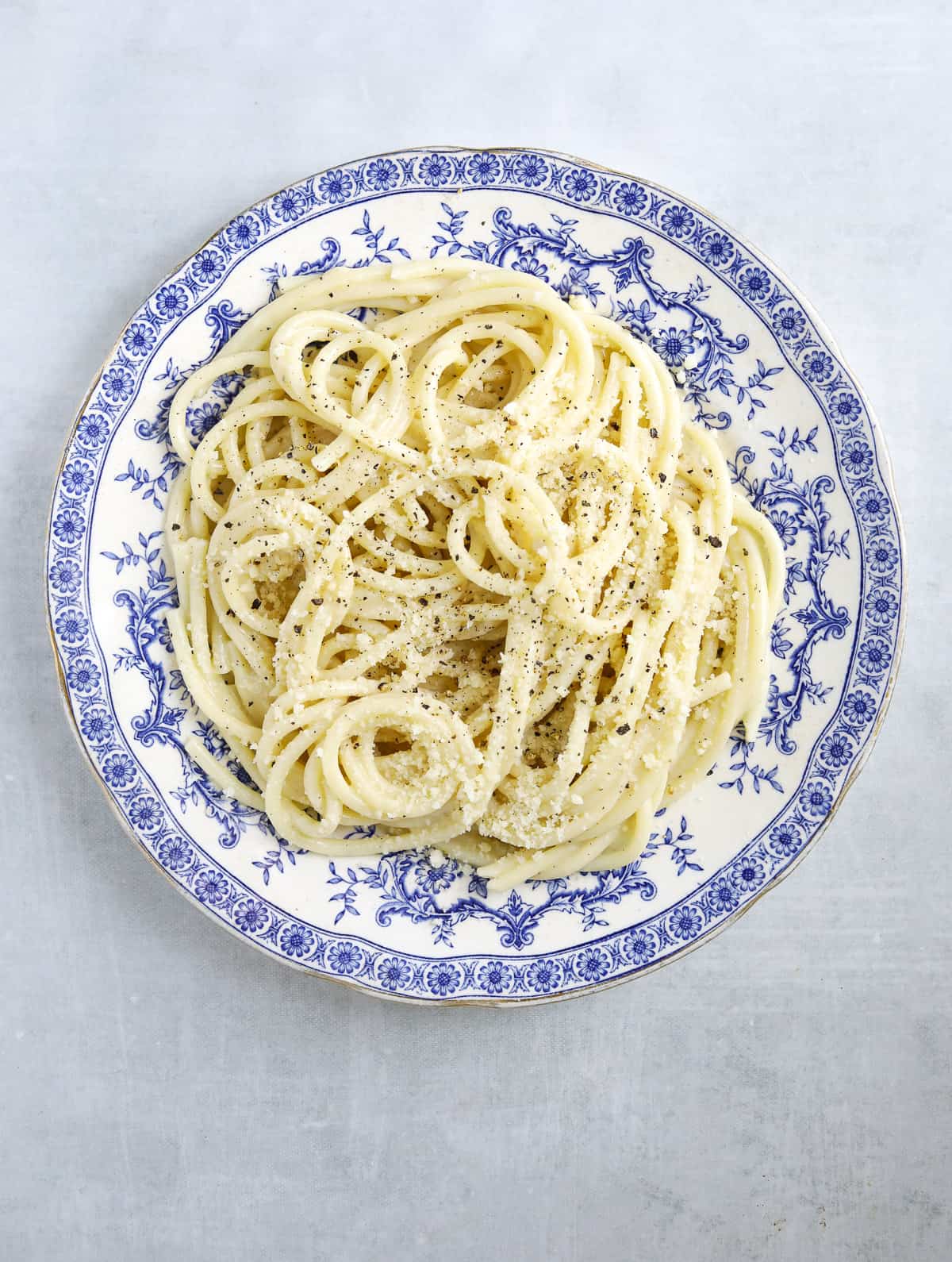 a vintage blue plate with a pile of cacio e pepe piled on top with cracked black pepper and parmesan cheese