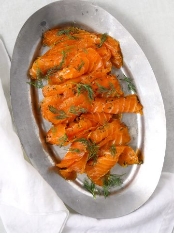 a silver plate of thinly sliced citrus cured salmon topped with fresh dil
