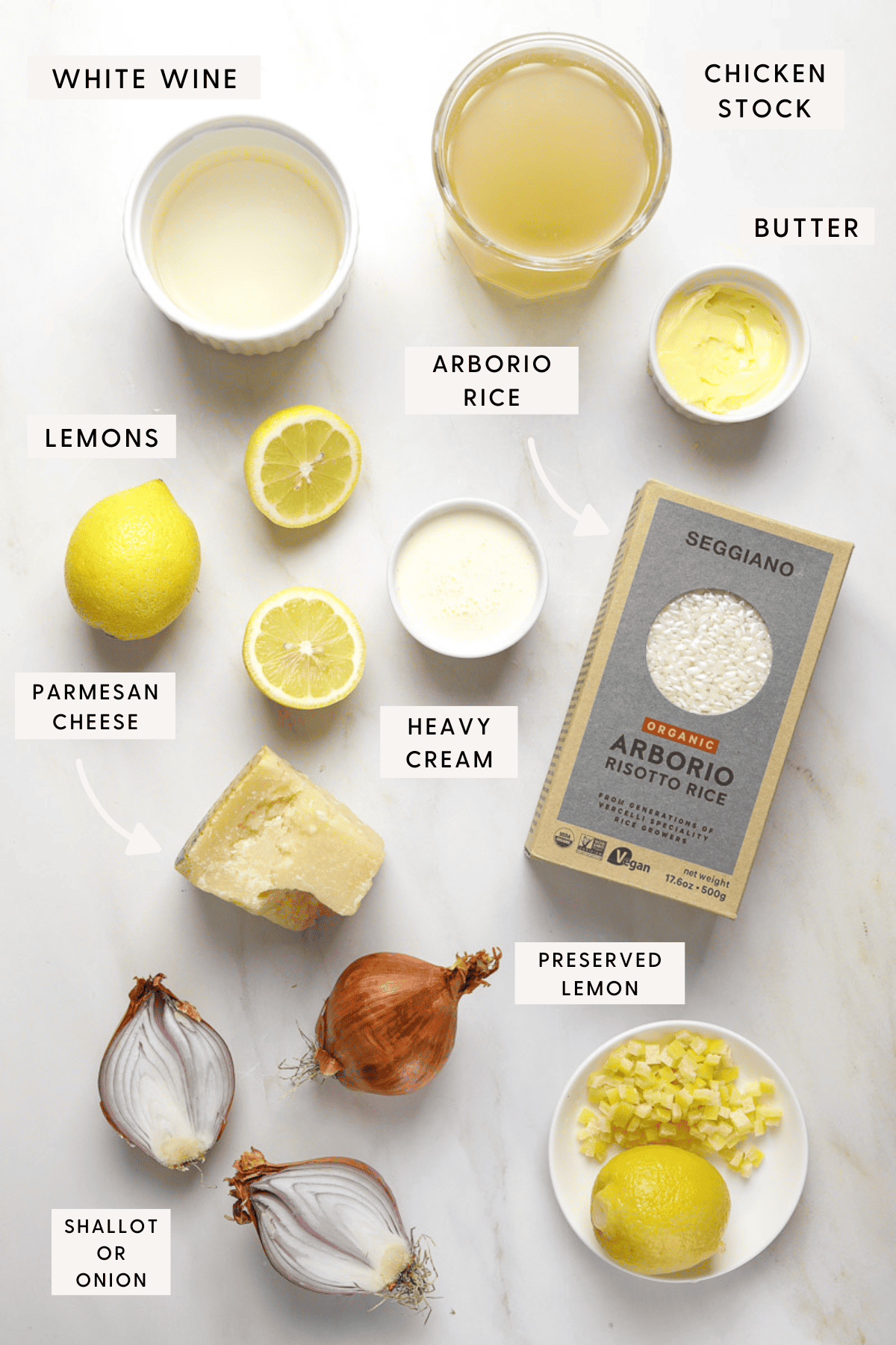 Ingredients for risotto individually portioned and labeled on a marble background. White wine, chicken stock, butter, lemons, arborio rice, shallot and parmesan cheese.