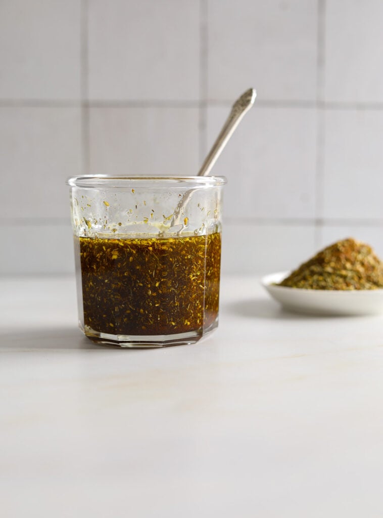 A jar filled with Za'atar oil and a silver spoon.