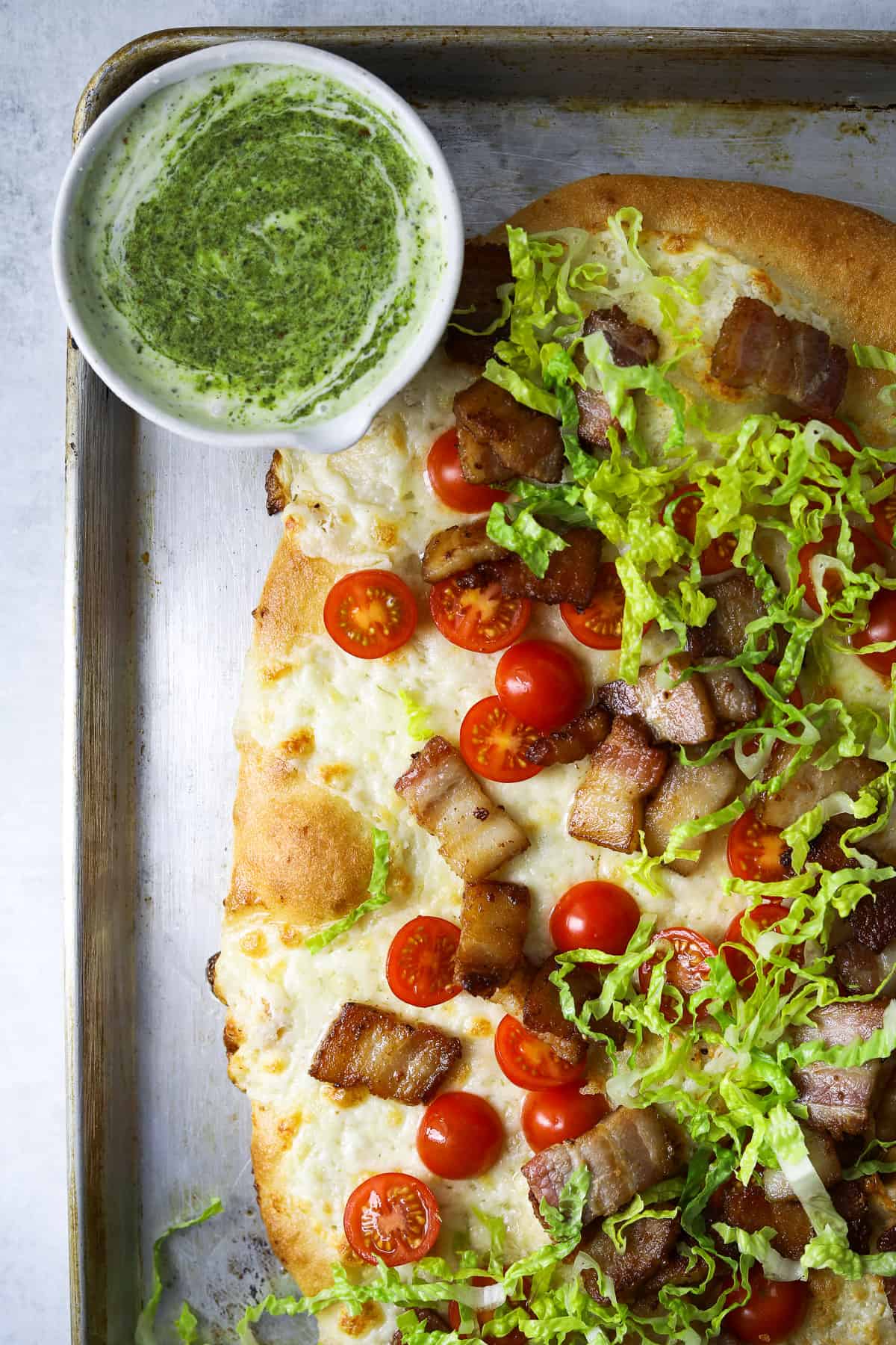 a baking tray with BLT pizza and a side dish of basil pesto ranch dipping sauce