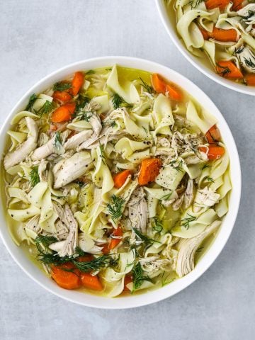 a large white bowl filled with Rotisserie Chicken Noodle Soup, fresh herb and egg noodles