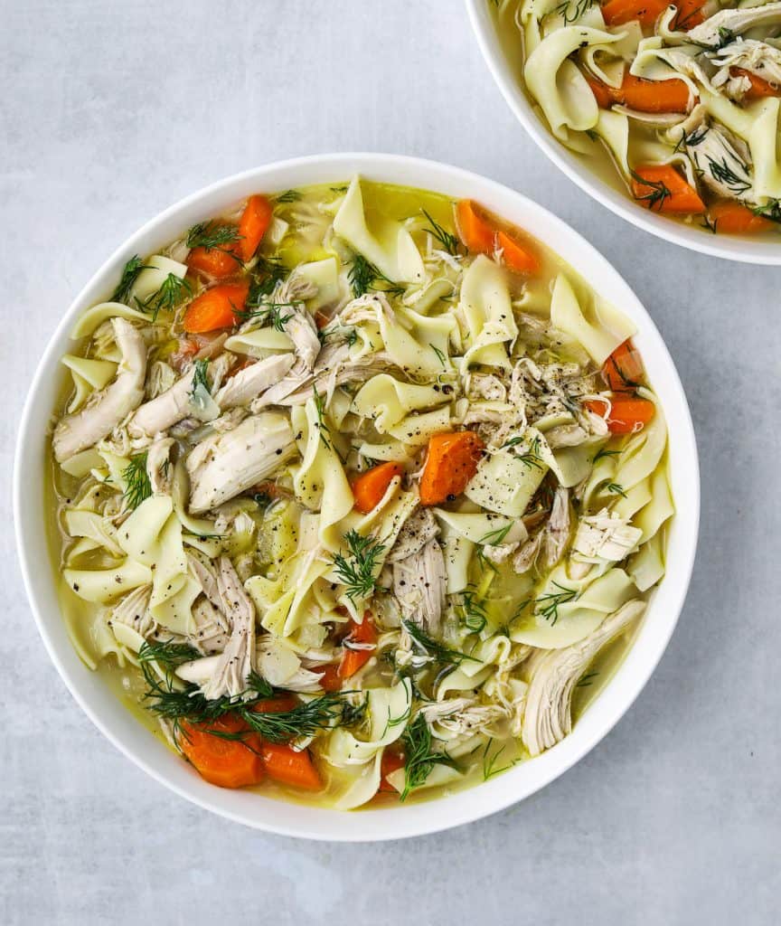 a large white bowl filled with Rotisserie Chicken Noodle Soup, fresh herb and egg noodles