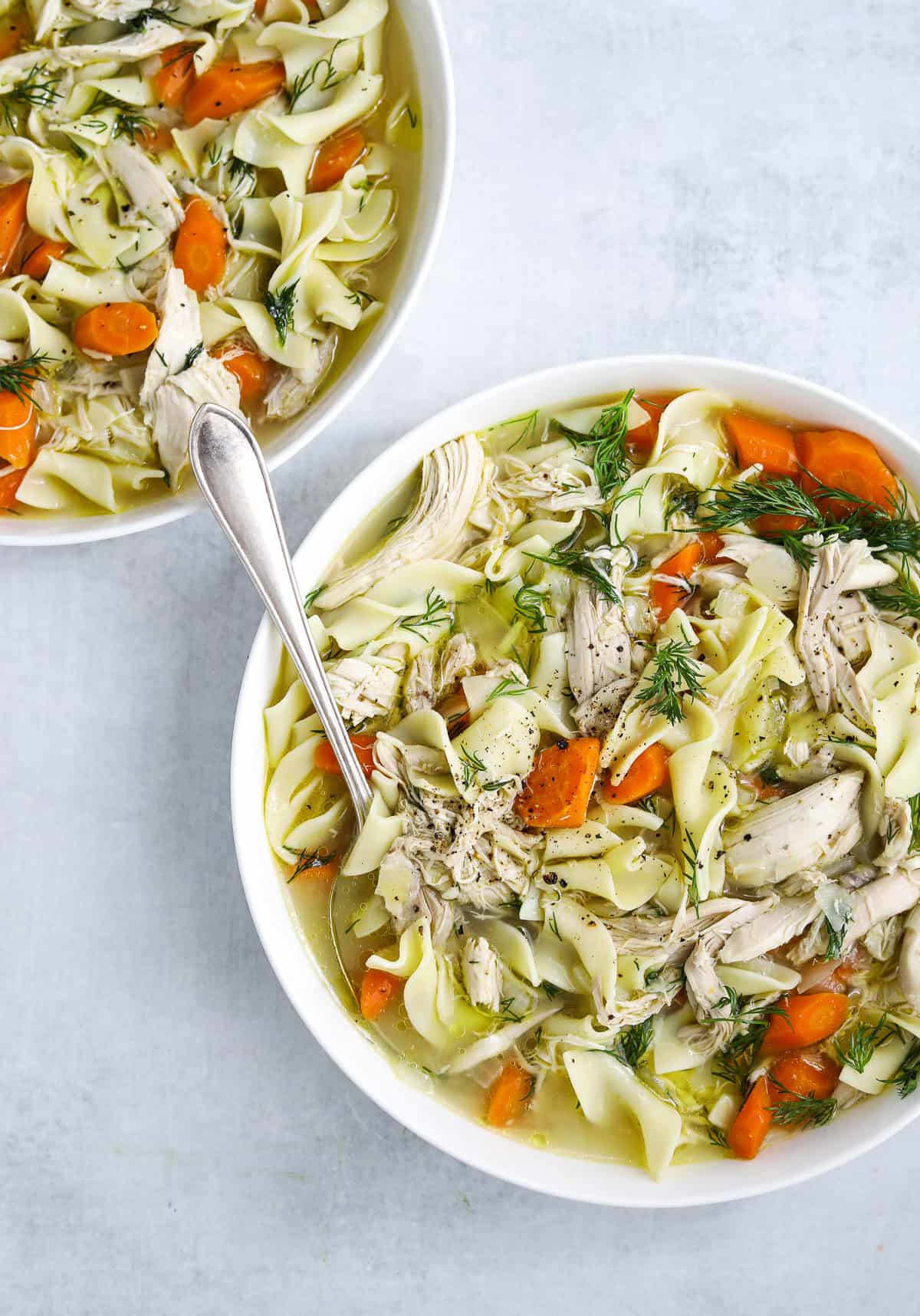 two white bowls of Rotisserie Chicken Noodle Soup one with a silver soup spoon