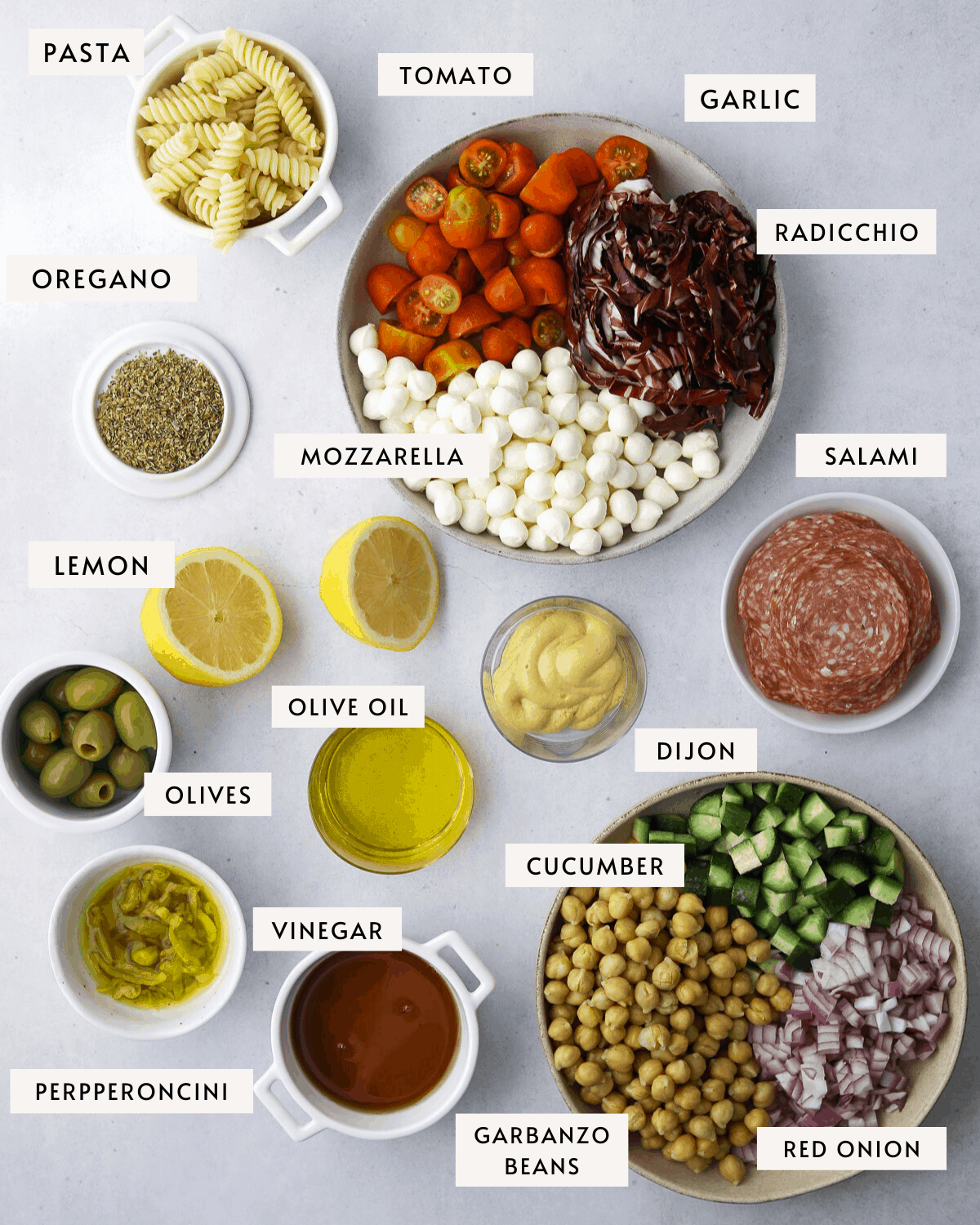 Italian Pasta Salad ingredients in individual bowls, olives, pasta, radicchio, tomatoes, salami, cucumber, garbanzo beans