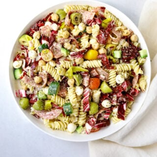 a large white bowl of Italian Pasta Salad with rotini pasta, olives, salami, mozzarella, cucumber and tomatoes