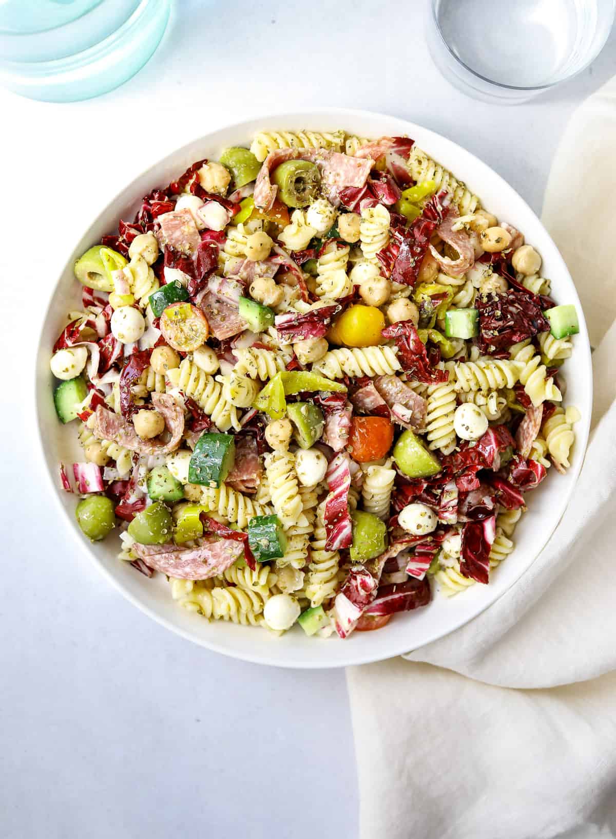 a large white bowl of Italian Pasta Salad with rotini pasta, olives, salami, mozzarella, cucumber and tomatoes