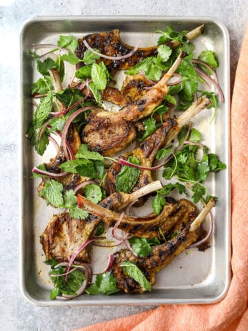a rectangular baking tray filled with grilled lamb chops, fresh herbs and red onion