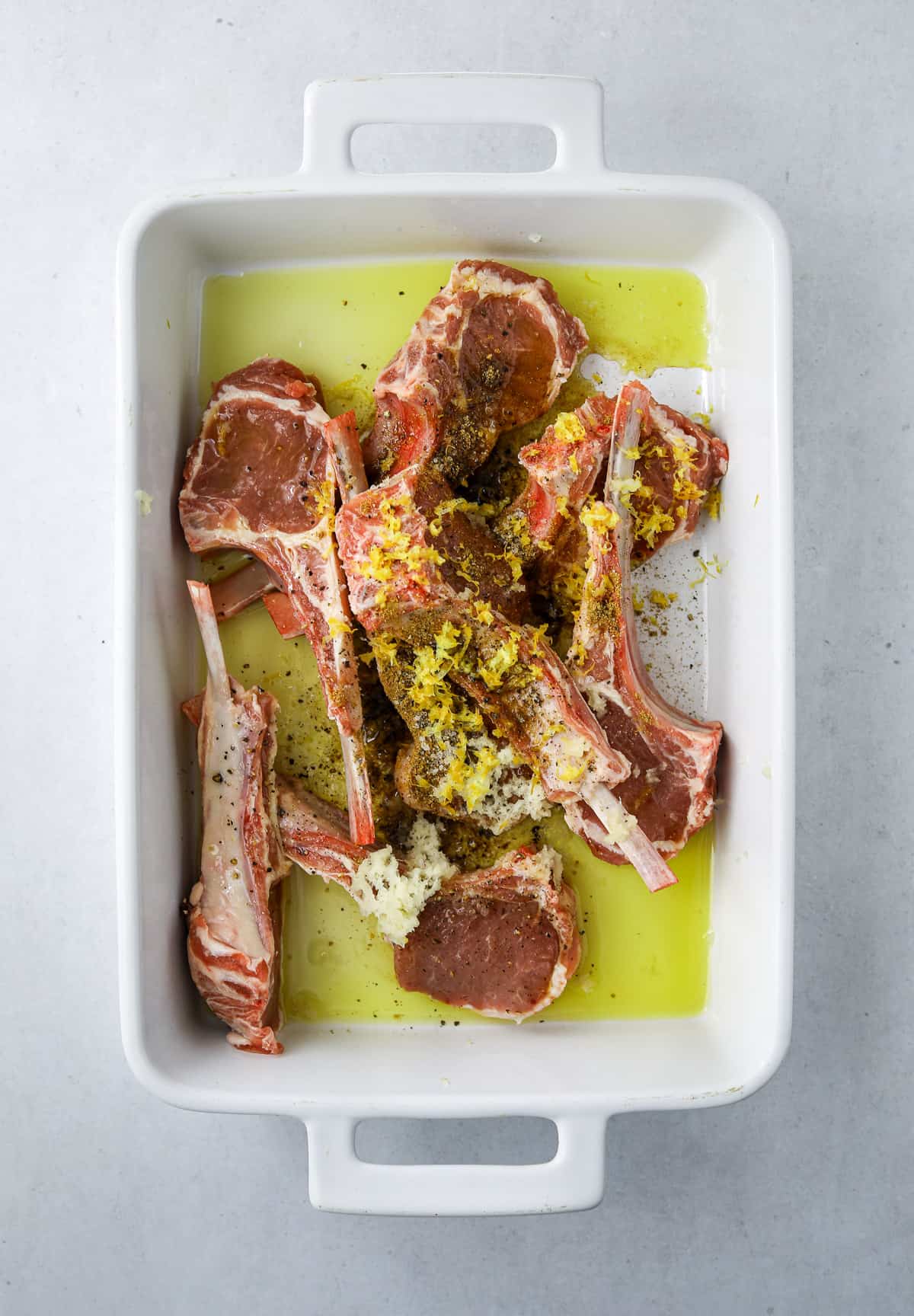 lamb chops marinating in olive oil in a  white ceramic baking dish
