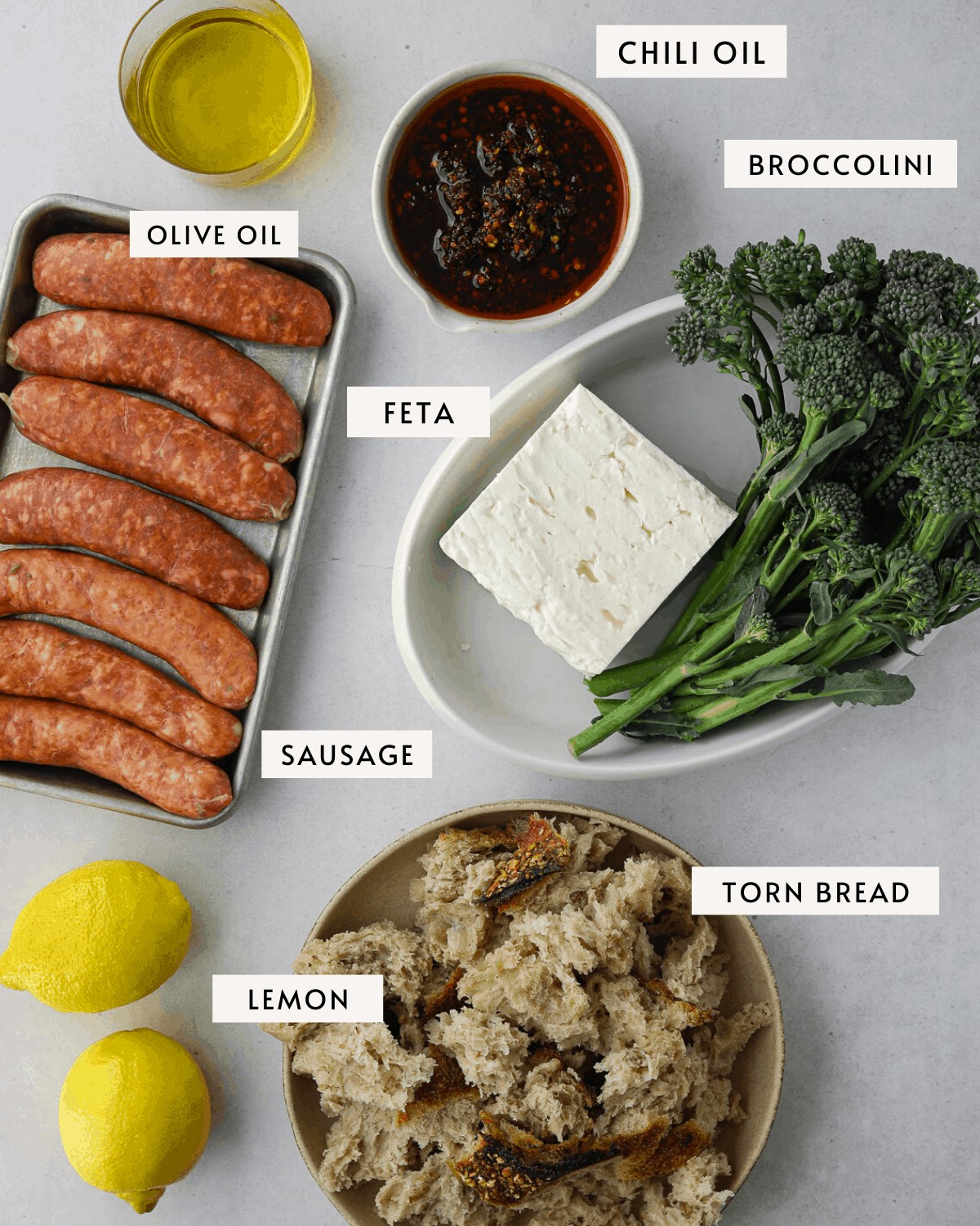 recipe ingredients raw sausages, a bunch of broccolini, a block of feta cheese, chili oil and bread