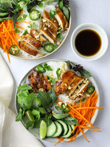 two bowls of Vietnamese rice noodle salad topped with basil, cilantro, mint and chicken