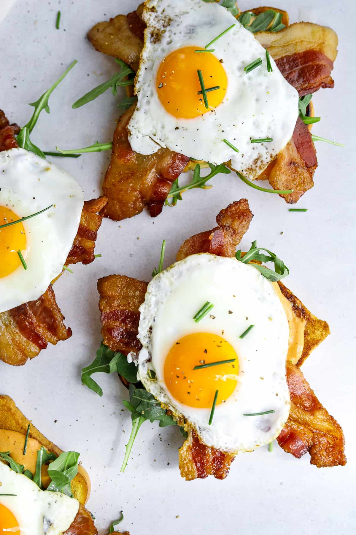 three breakfast toasts topped with sunny side up eggs and chives