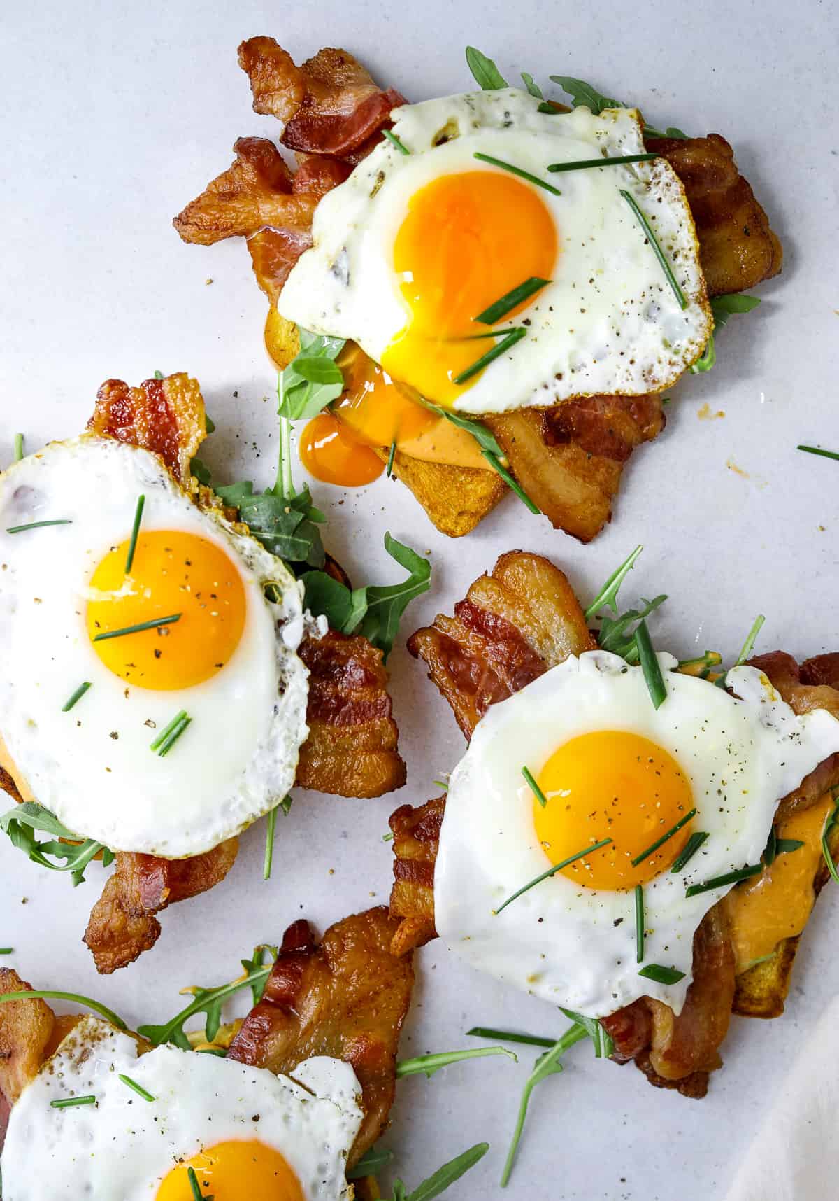 three breakfast toasts with sunny side up eggs and a broken runny egg yolk