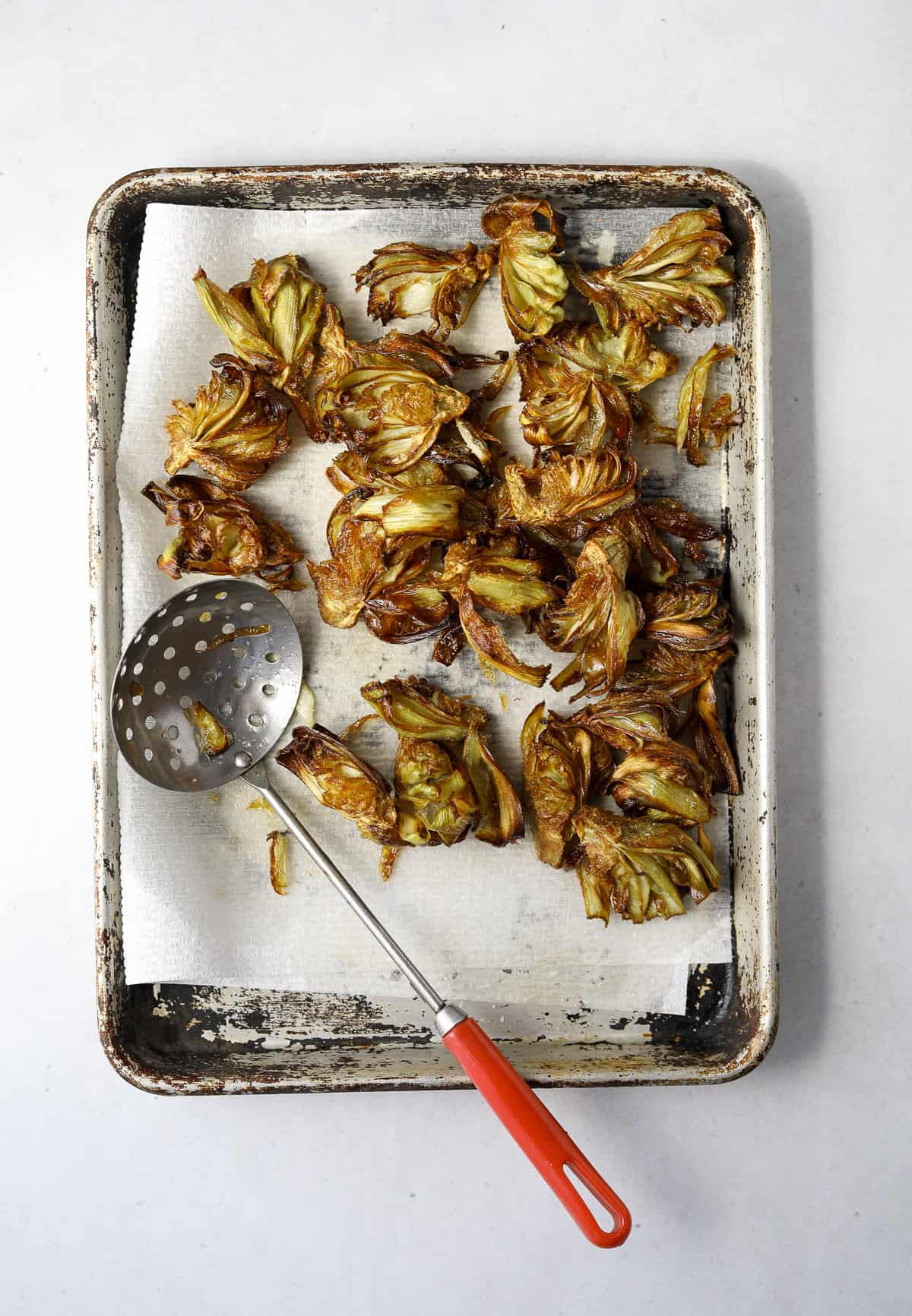 fried artichokes draining on a paper towel lined baking tray