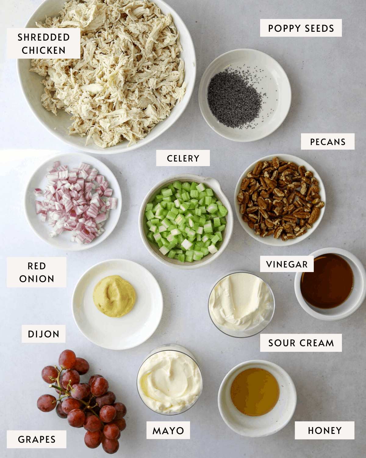 Sonoma Chicken Salad ingredients in individual bowls, shredded chicken, diced red onion, celery, grapes, toasted pecans, mayo etc