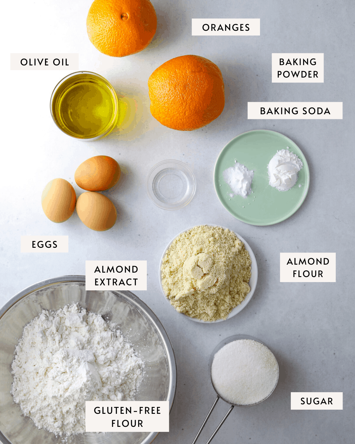 olive oil cake ingredients individually portioned, two oranges, three eggs, baking soda, baking powder, a white dish of almond flour etc..