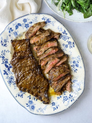 a blue and white platter filled with grilled skirt steak with a bowl of salad on the side