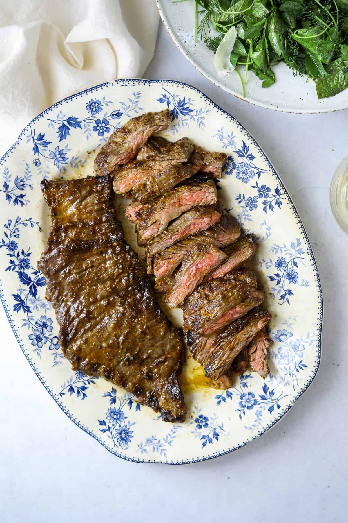 a blue and white platter filled with grilled skirt steak with a bowl of salad on the side