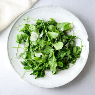 a white ceramic bowl filled with fresh herb salad with shaved parmesan cheese.