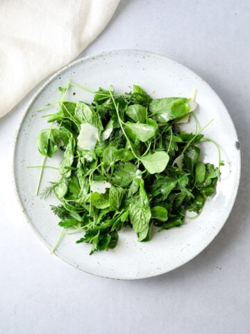 a white ceramic bowl filled with fresh herb salad with shaved parmesan cheese.