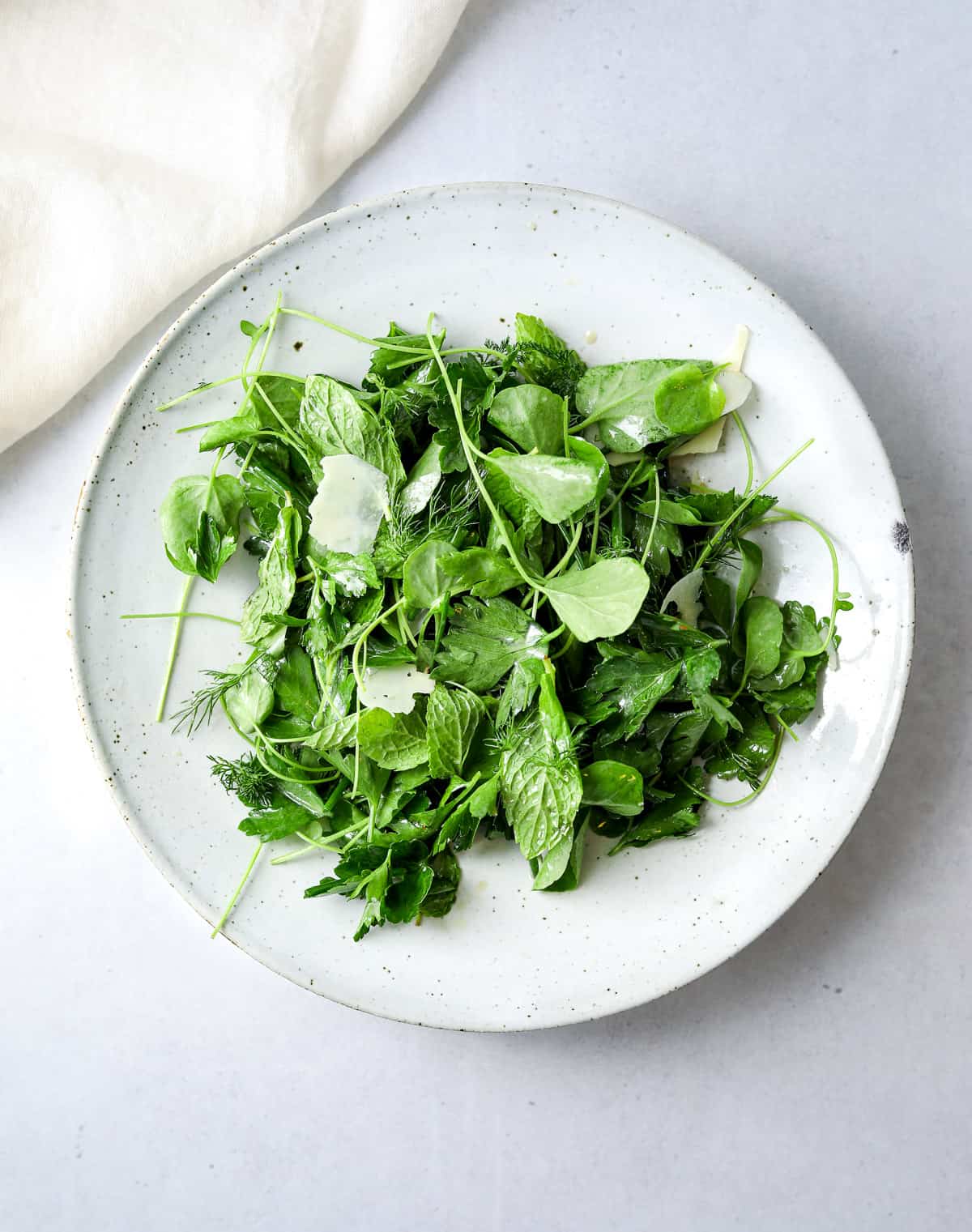 a white ceramic bowl filled with fresh herb salad with shaved parmesan cheese. 