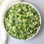 a white bowl filled with spring couscous salad, diced avocado, cucumber and fresh herbs.