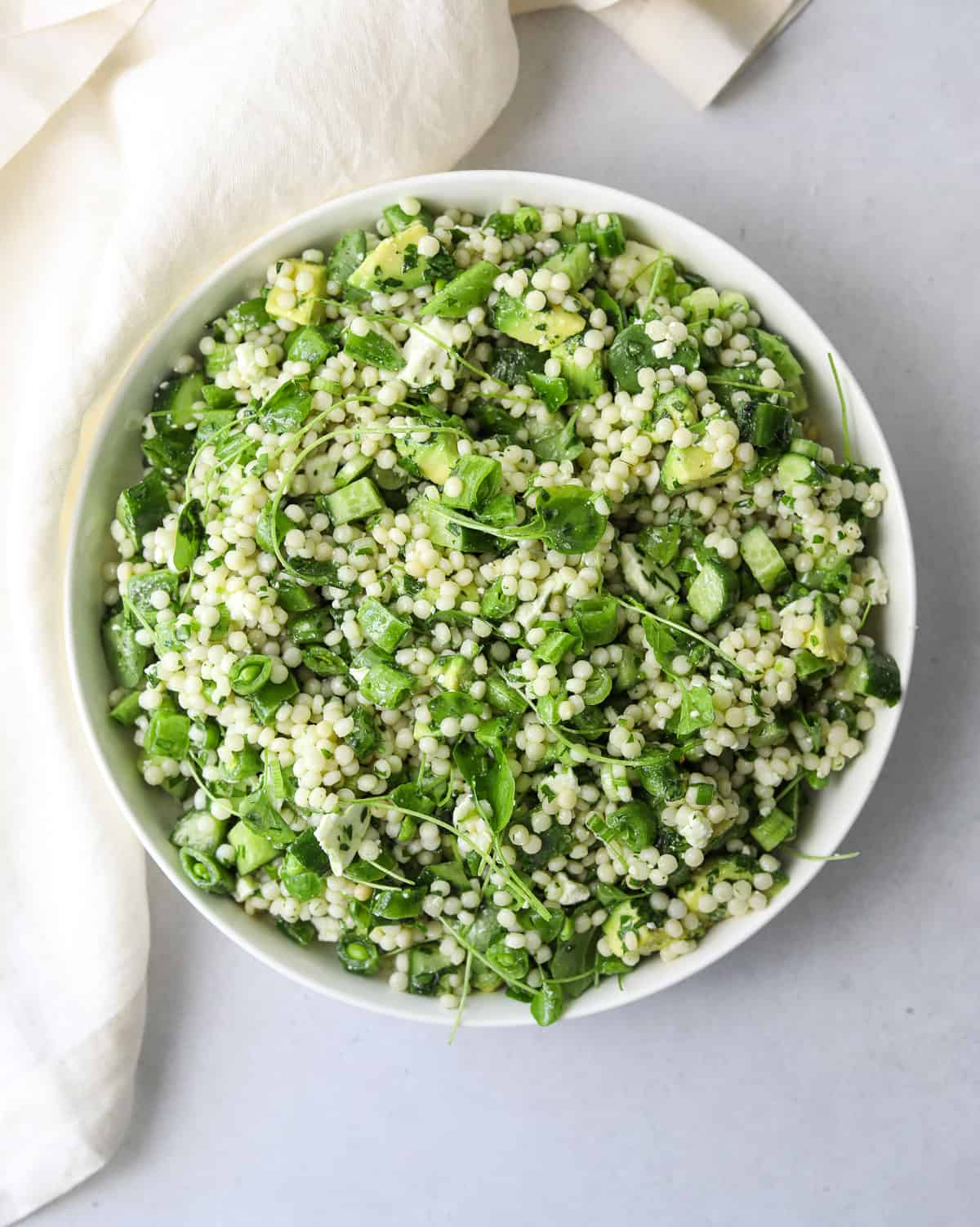 a white bowl filled with spring couscous salad, diced avocado, cucumber and fresh herbs. 