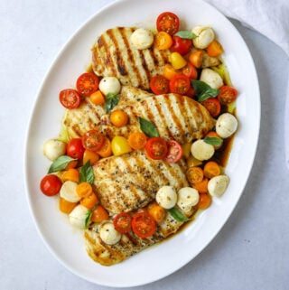 a round oval platter filled with grilled chicken breast topped with cherry tomatoes, mozzarella and fresh basil.