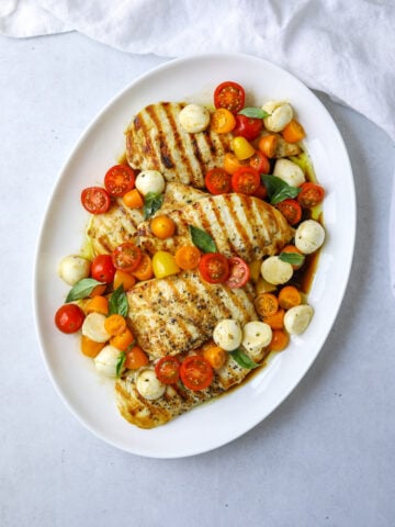 a round oval platter filled with grilled chicken breast topped with cherry tomatoes, mozzarella and fresh basil.