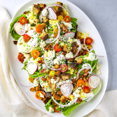 a bright and colorful little gem salad topped with cherry tomatoes, blue cheese dressing, croutons and radish on a white platter oval