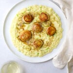 a white plate with creamy corn porridge, 5 seared scallops and thinly sliced green onion